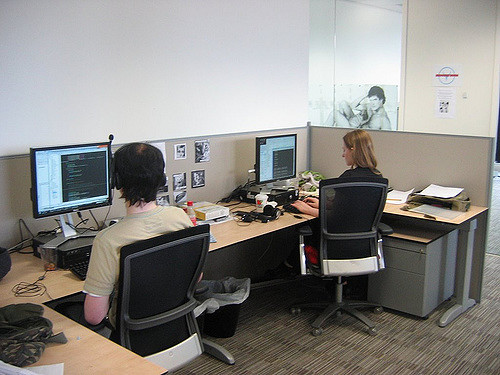 Photo of two people in a cubicle working on computers.